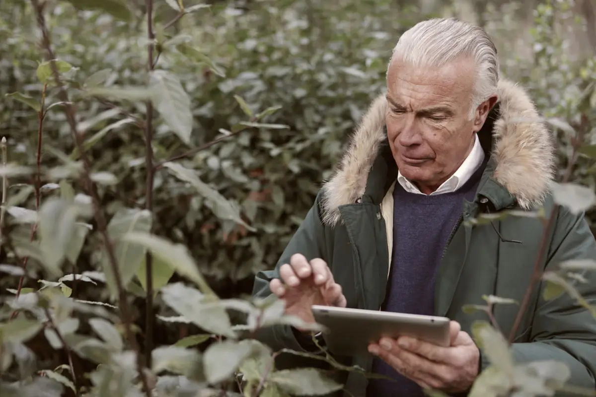 Man met een tablet in zijn handen tussen jonge bomen en struiken