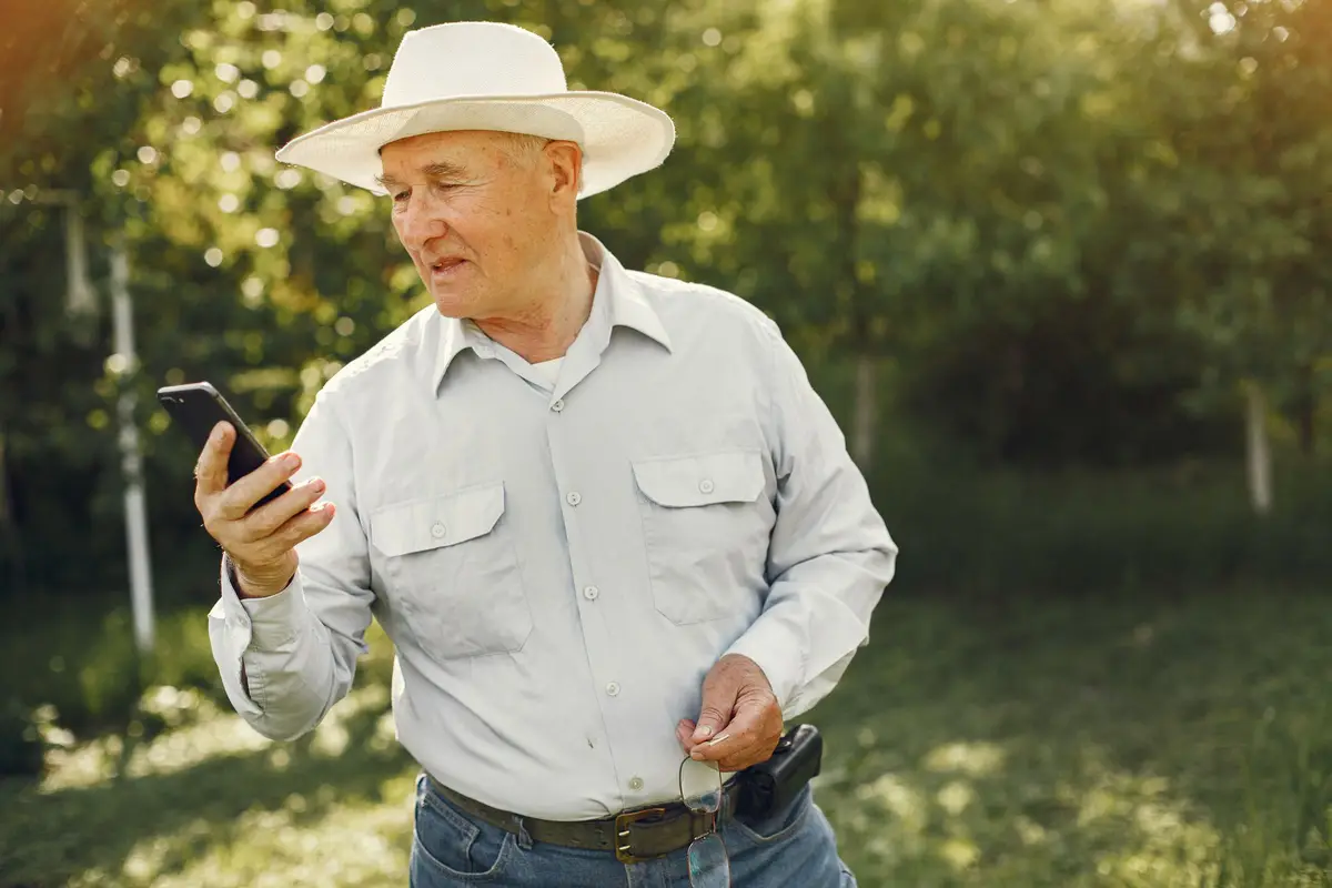 Boer met een strohoed kijkt op zijn telefoon, met het groen achter hem